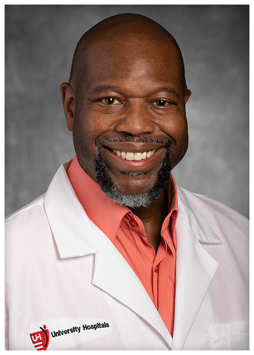 A smiling middle-aged Black man wearing a white lab coat with the University Hospitals logo.