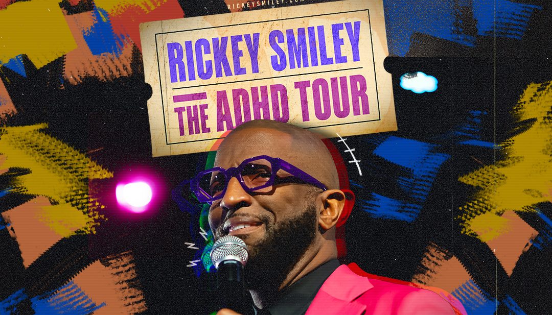 A man wearing colorful glasses and a pink suit stands on stage holding a microphone, promoting "Rickey Smiley: The ADHD Tour" at Playhouse Square in Cleveland, Ohio on September 11.